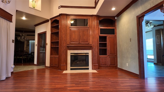 unfurnished living room featuring built in shelves, a premium fireplace, wood finished floors, a ceiling fan, and ornamental molding