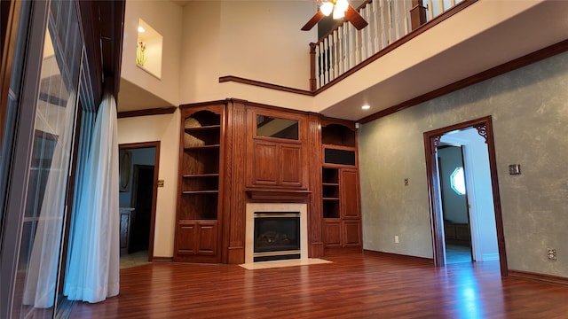 unfurnished living room featuring a fireplace with flush hearth, a high ceiling, baseboards, and wood finished floors