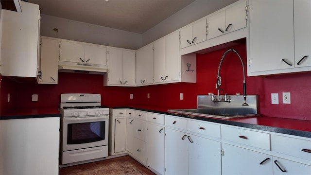 kitchen featuring gas range gas stove, dark countertops, white cabinets, a sink, and under cabinet range hood