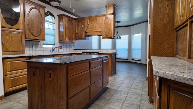 kitchen with brown cabinets, crown molding, decorative backsplash, a kitchen island, and a sink