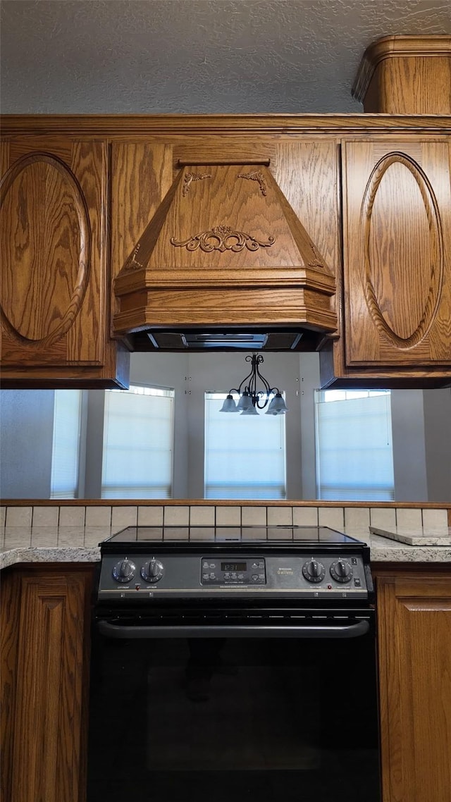 kitchen featuring custom exhaust hood, black / electric stove, brown cabinetry, and light countertops