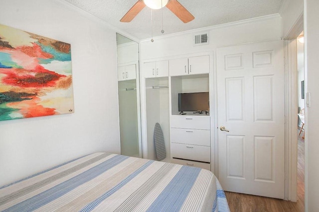 bedroom with visible vents, dark wood-type flooring, a textured ceiling, crown molding, and a closet