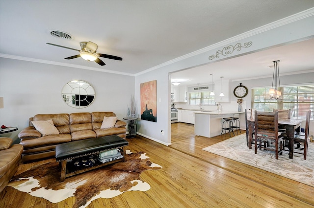 living area with crown molding, a ceiling fan, visible vents, and light wood-style floors