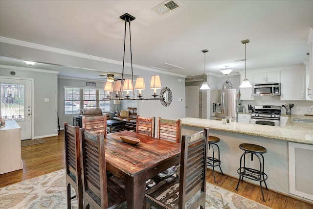 dining room featuring light wood-type flooring, visible vents, a ceiling fan, and ornamental molding