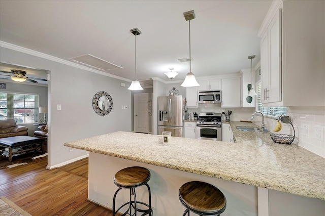 kitchen with a peninsula, a sink, appliances with stainless steel finishes, light stone countertops, and light wood finished floors