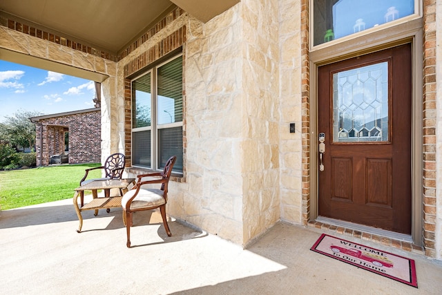 view of exterior entry with stone siding, covered porch, and a yard