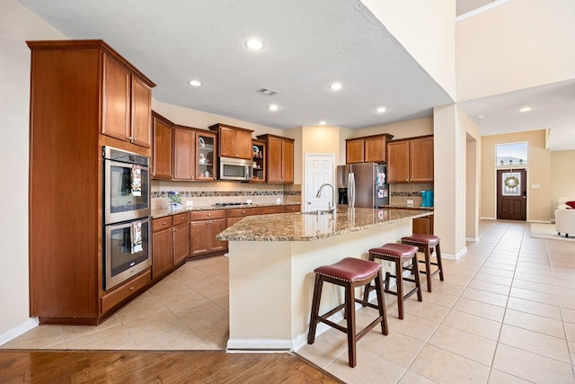 kitchen featuring stainless steel appliances, brown cabinetry, and light tile patterned flooring