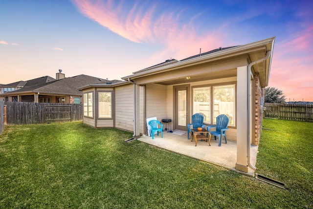 back of property at dusk featuring a patio, a lawn, and a fenced backyard