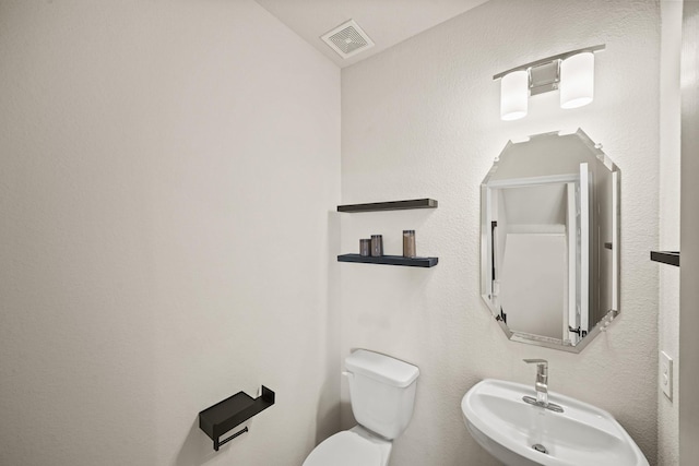 half bath featuring toilet, visible vents, and a sink