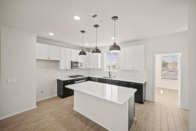 kitchen featuring light wood finished floors, visible vents, stainless steel microwave, a center island, and white cabinetry