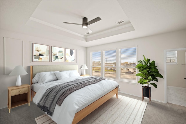 bedroom featuring a tray ceiling, carpet, visible vents, a ceiling fan, and baseboards