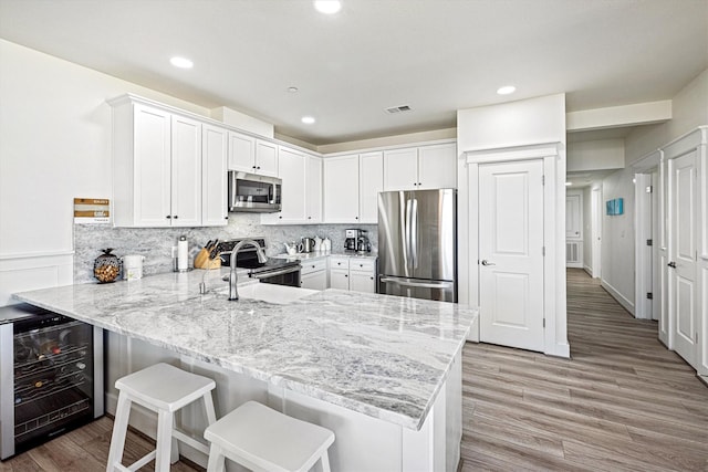 kitchen with beverage cooler, a peninsula, visible vents, white cabinetry, and appliances with stainless steel finishes