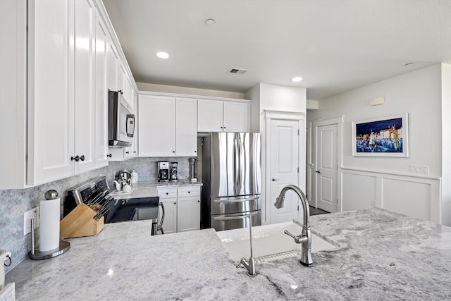 kitchen featuring light stone counters, white cabinetry, stainless steel appliances, and a sink