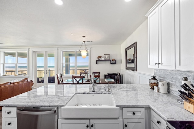 kitchen with a sink, hanging light fixtures, stainless steel dishwasher, and light stone countertops