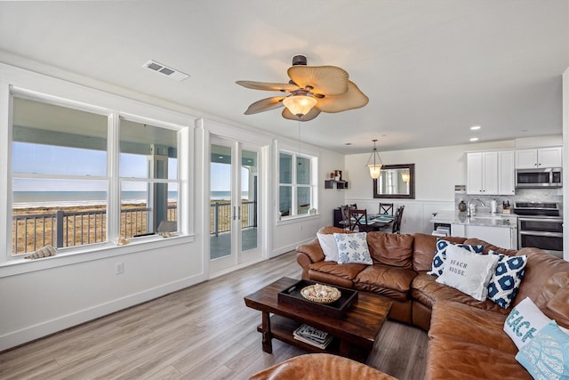 living room with light wood-style floors, ceiling fan, visible vents, and baseboards