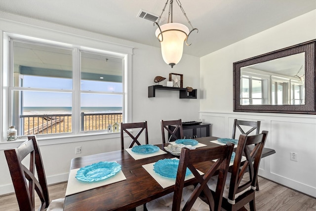 dining room with light wood-type flooring, a wainscoted wall, a decorative wall, and visible vents