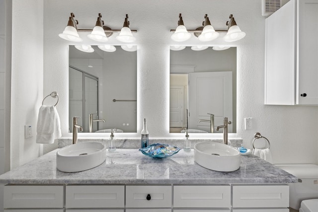 full bathroom with visible vents, a sink, a shower stall, and double vanity