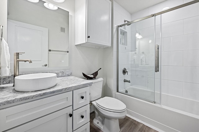 bathroom featuring visible vents, toilet, wood finished floors, combined bath / shower with glass door, and vanity