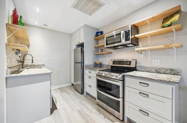 kitchen with visible vents, light stone counters, stainless steel appliances, open shelves, and a sink