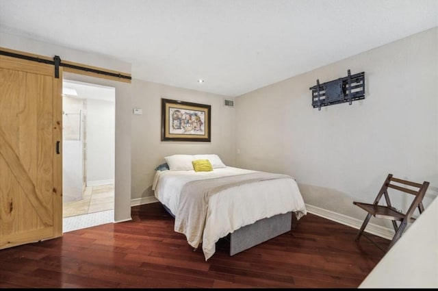 bedroom with baseboards, a barn door, visible vents, and wood finished floors