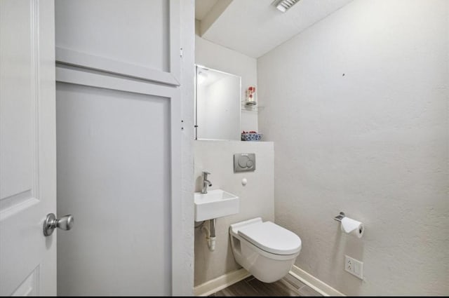 half bath featuring visible vents, toilet, a sink, wood finished floors, and baseboards