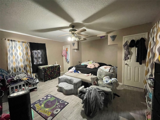 bedroom featuring ceiling fan, a textured ceiling, baseboards, and wood finished floors