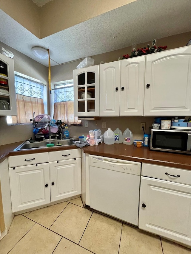 kitchen with white dishwasher, a sink, white cabinets, stainless steel microwave, and dark countertops