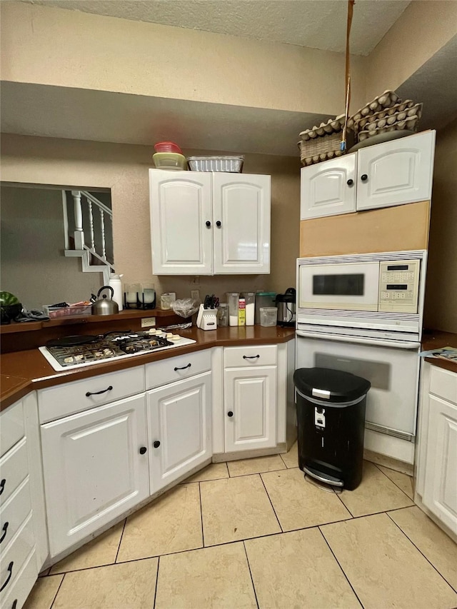 kitchen with light tile patterned floors, white appliances, dark countertops, and white cabinetry