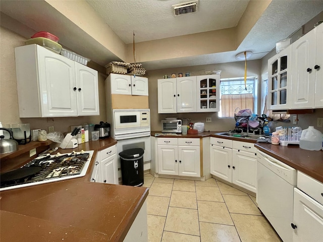 kitchen with white appliances, visible vents, dark countertops, glass insert cabinets, and a sink