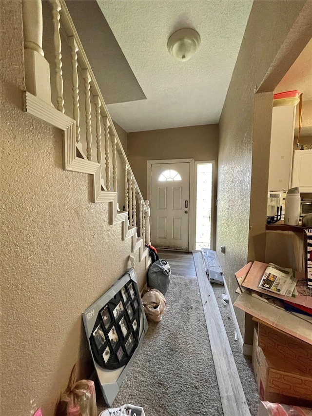 foyer entrance with wood finished floors, a textured wall, a textured ceiling, and stairs