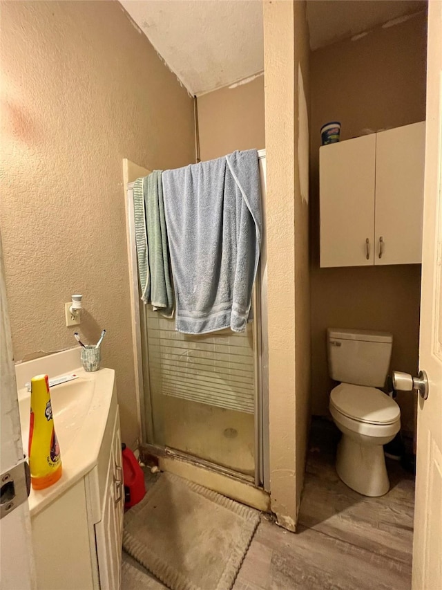 full bath featuring a textured wall, a shower stall, toilet, and wood finished floors