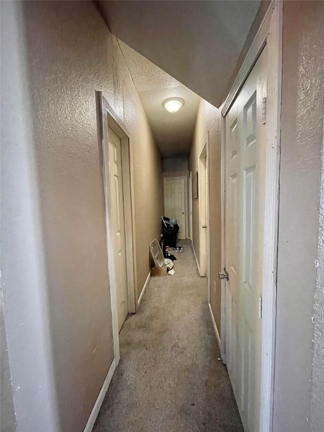 hallway with a textured ceiling, a textured wall, and baseboards