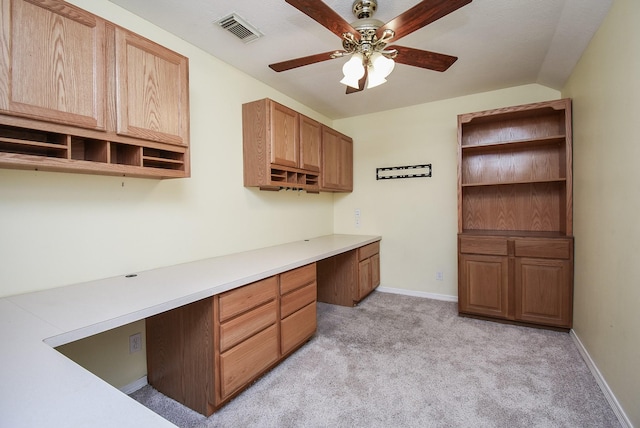 unfurnished office with built in desk, visible vents, light carpet, ceiling fan, and baseboards