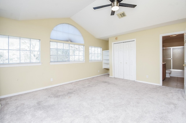 unfurnished bedroom with carpet, a closet, visible vents, ensuite bathroom, and vaulted ceiling