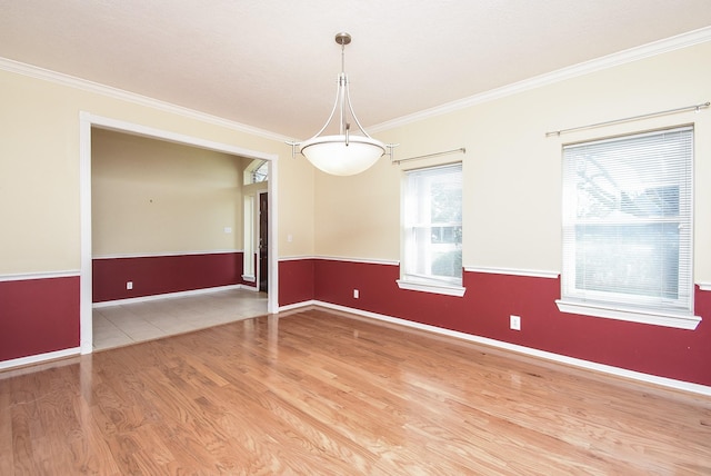 empty room featuring a wainscoted wall, baseboards, wood finished floors, and crown molding