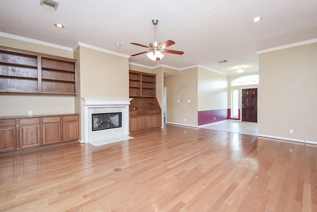 unfurnished living room featuring light wood-style flooring, a fireplace with flush hearth, visible vents, baseboards, and ornamental molding