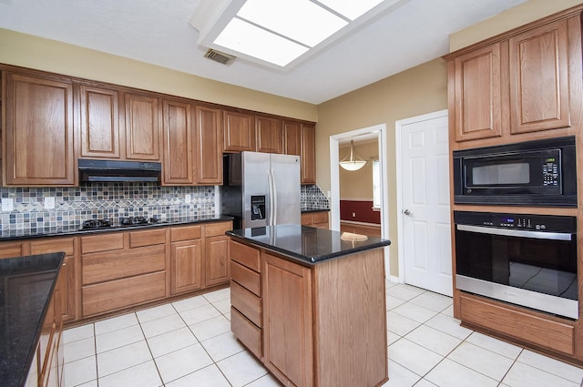 kitchen with light tile patterned flooring, under cabinet range hood, visible vents, decorative backsplash, and black appliances