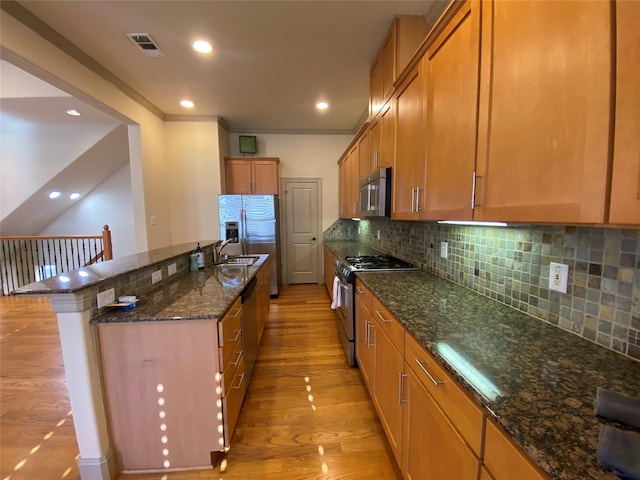 kitchen featuring visible vents, dark stone counters, light wood-style flooring, stainless steel appliances, and backsplash