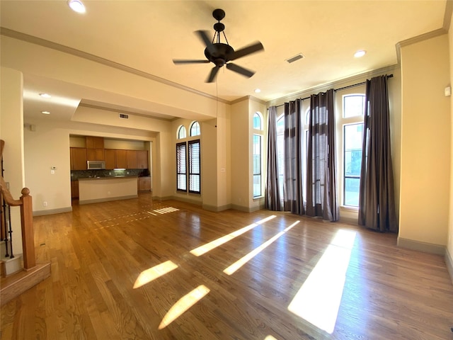 unfurnished living room featuring light wood finished floors, baseboards, visible vents, and ornamental molding