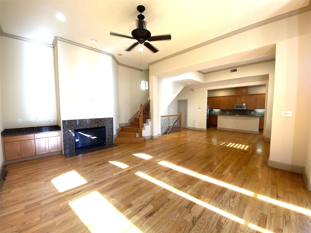 unfurnished living room featuring ornamental molding, visible vents, a tiled fireplace, and light wood finished floors