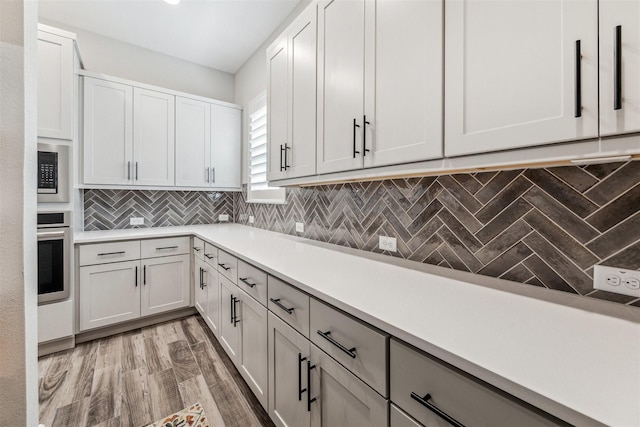 kitchen featuring light wood-style flooring, built in microwave, light countertops, stainless steel oven, and backsplash