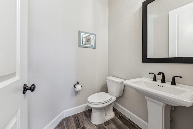 bathroom with wood tiled floor, baseboards, a sink, and toilet