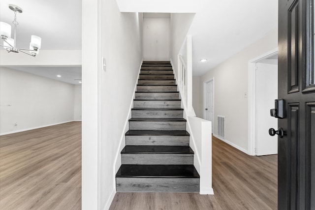 stairs with baseboards, wood finished floors, visible vents, and a notable chandelier