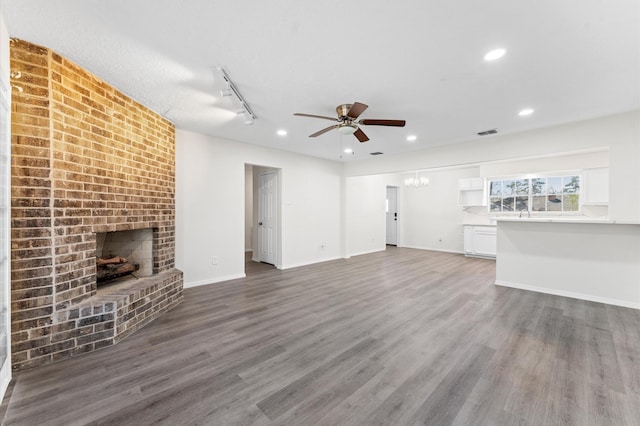 unfurnished living room featuring recessed lighting, ceiling fan with notable chandelier, wood finished floors, baseboards, and a brick fireplace