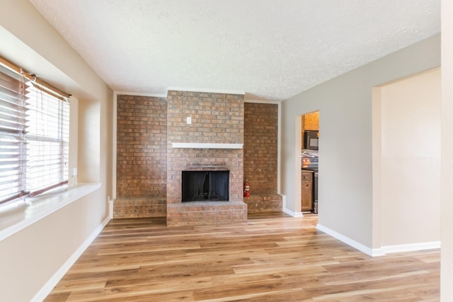 unfurnished living room with baseboards, a fireplace, a textured ceiling, and light wood finished floors