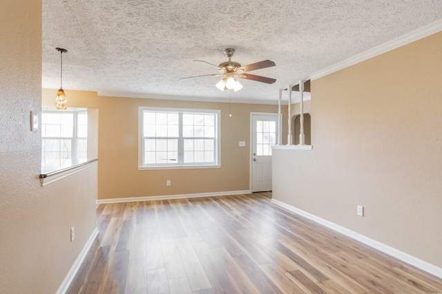 spare room with a textured ceiling, wood finished floors, a ceiling fan, baseboards, and crown molding