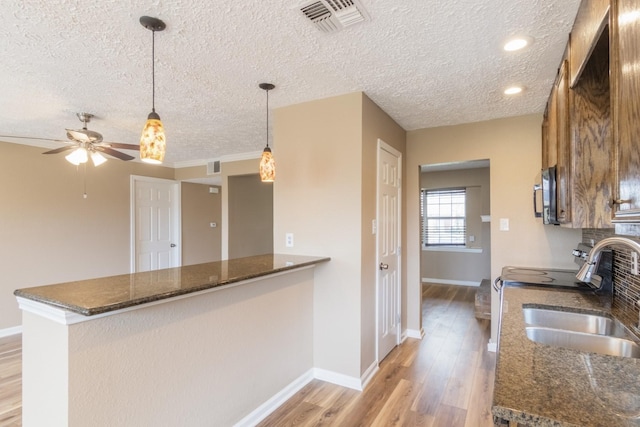 kitchen featuring decorative light fixtures, light wood finished floors, visible vents, a sink, and a peninsula