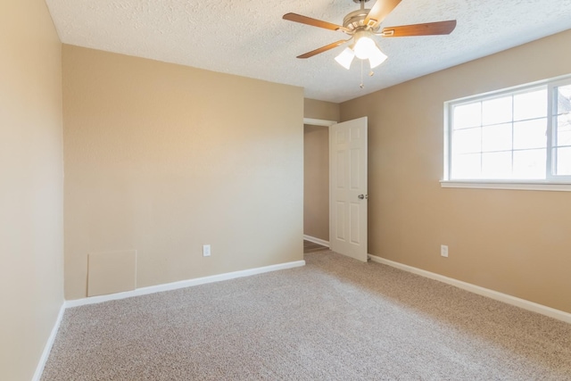 carpeted empty room with a textured ceiling, a ceiling fan, and baseboards