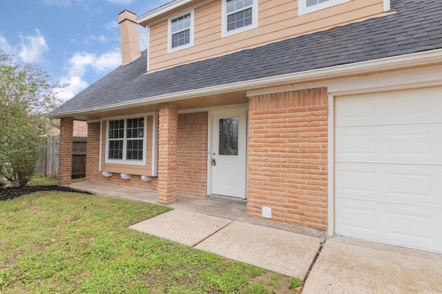 entrance to property with a garage, a shingled roof, a lawn, and brick siding