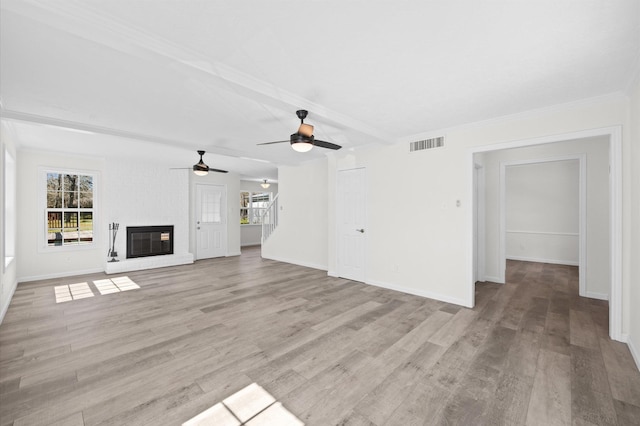 unfurnished living room featuring a brick fireplace, visible vents, plenty of natural light, and beamed ceiling